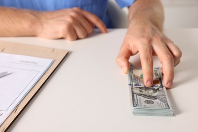 Photo of Corruption concept. Doctor with dollar banknotes at white table, closeup