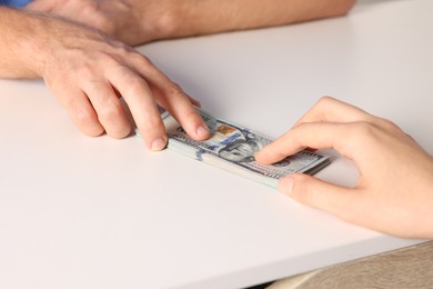 Photo of Corruption concept. Woman giving dollar banknotes to man at white table, closeup