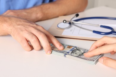 Photo of Corruption concept. Woman giving dollar banknotes to doctor at white table, closeup