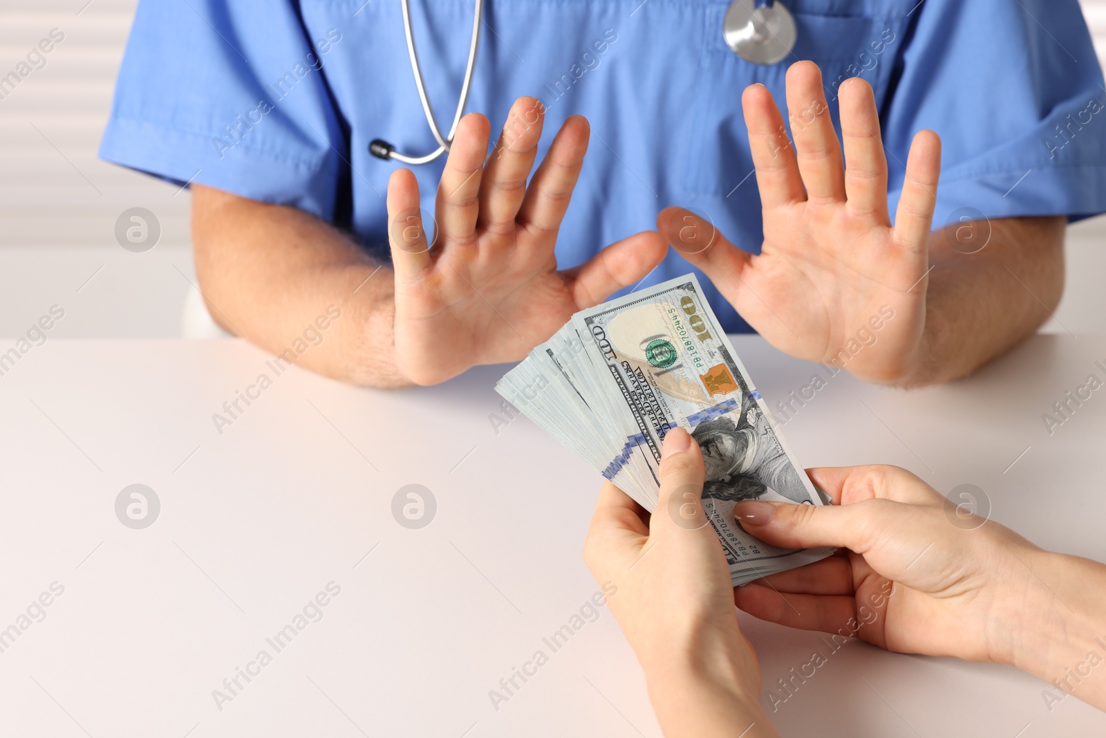 Photo of Corruption concept. Woman giving dollar banknotes to doctor at white table, closeup