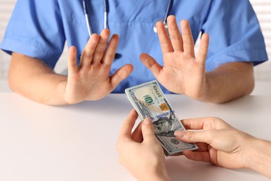 Photo of Corruption concept. Woman giving dollar banknotes to doctor at white table, closeup