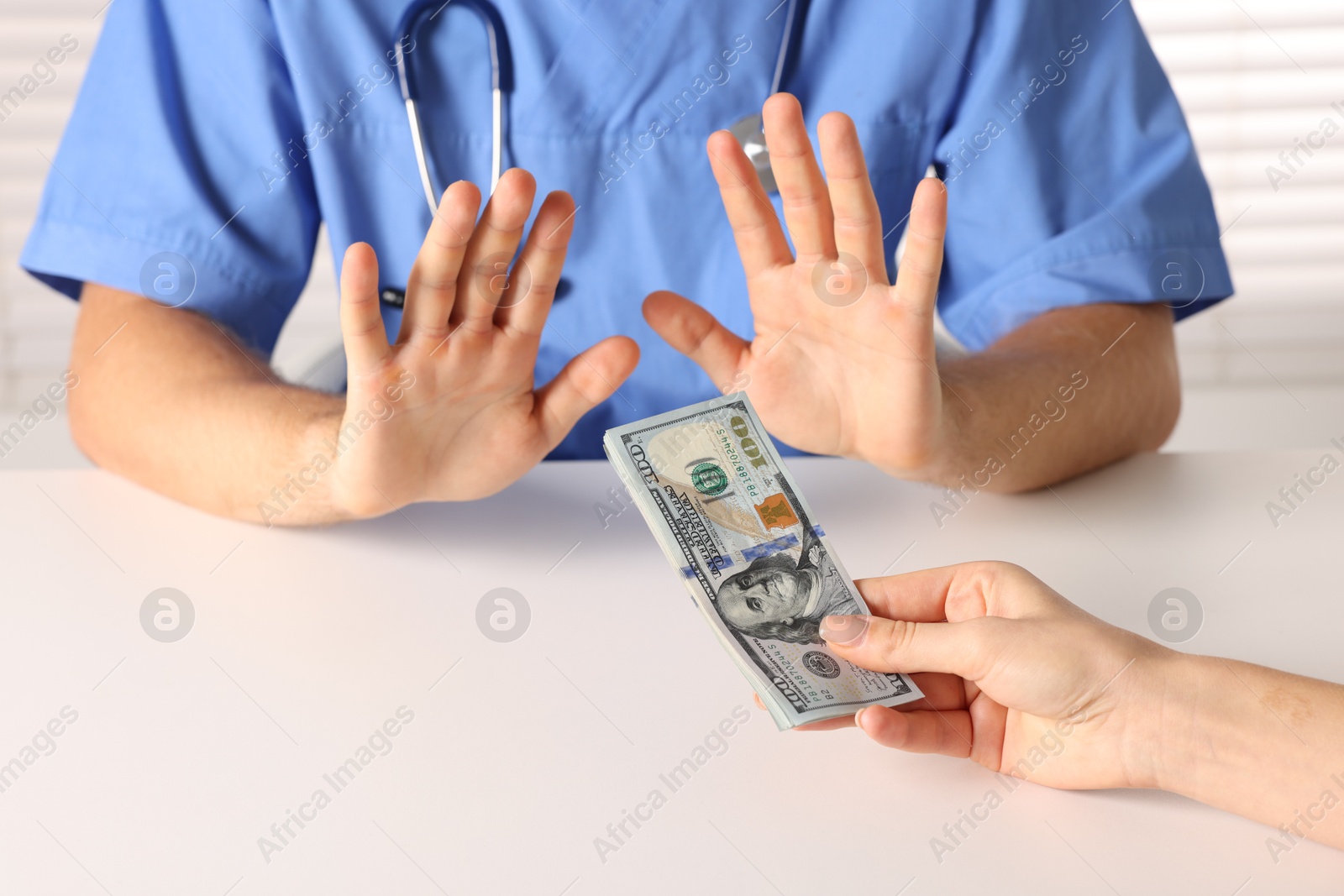 Photo of Corruption concept. Woman giving dollar banknotes to doctor at white table, closeup