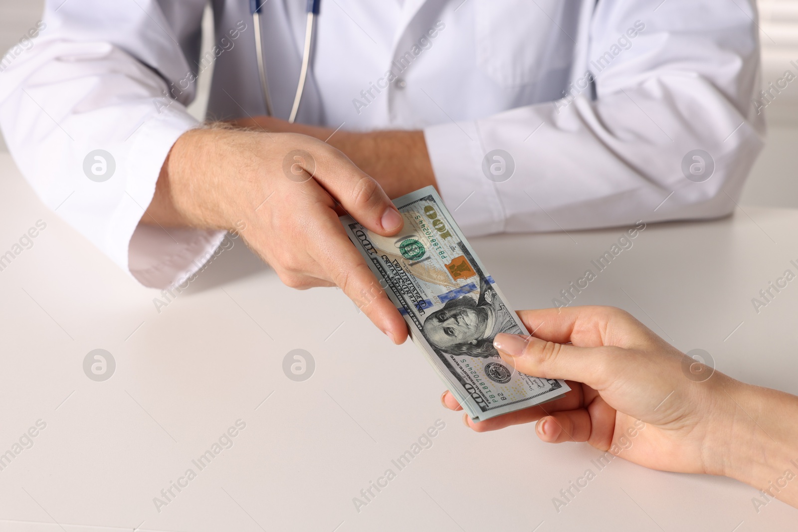 Photo of Corruption concept. Woman giving dollar banknotes to doctor at white table, closeup