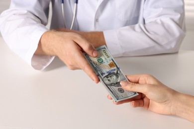 Photo of Corruption concept. Woman giving dollar banknotes to doctor at white table, closeup