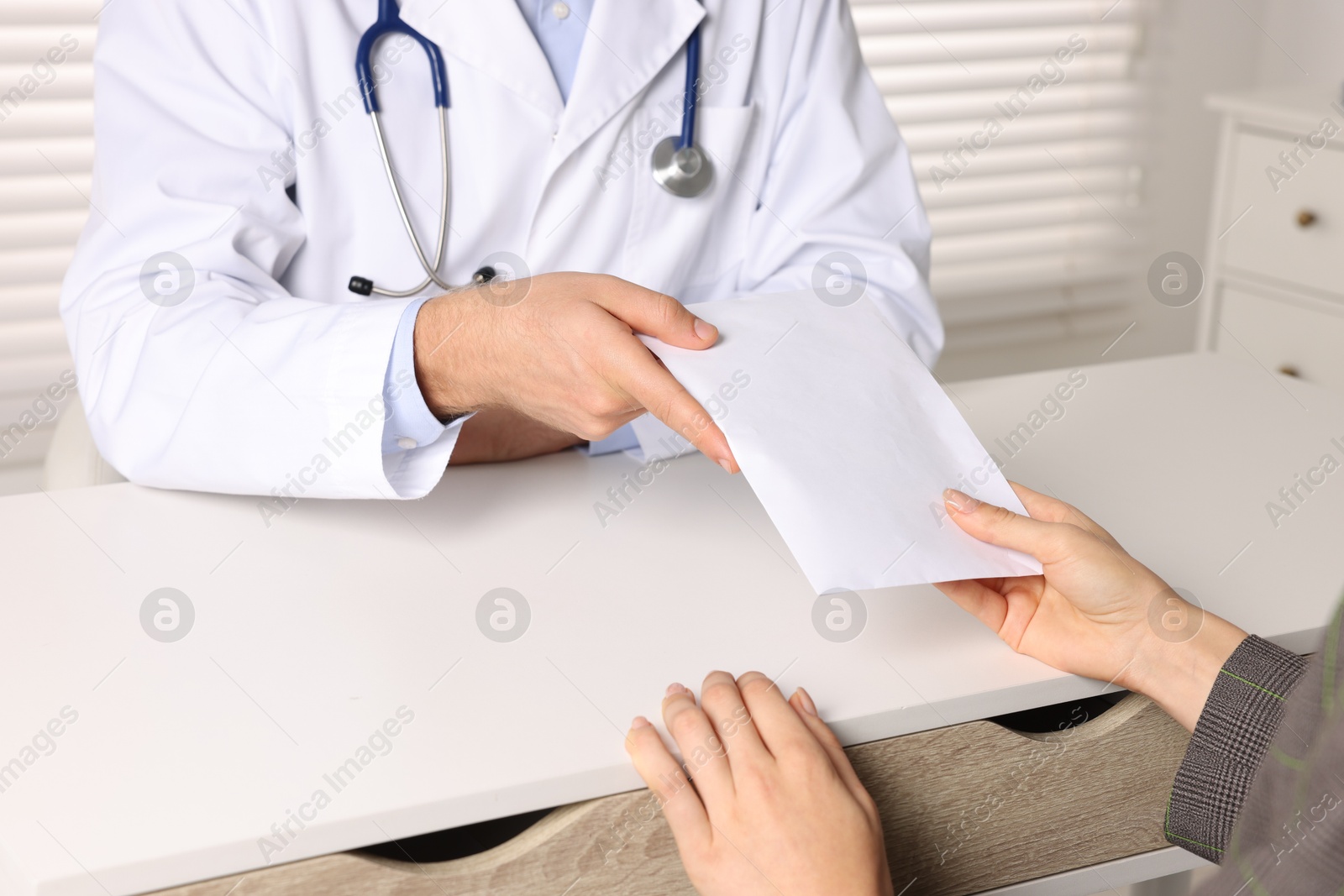 Photo of Corruption concept. Woman giving envelope with money to doctor at white table, closeup