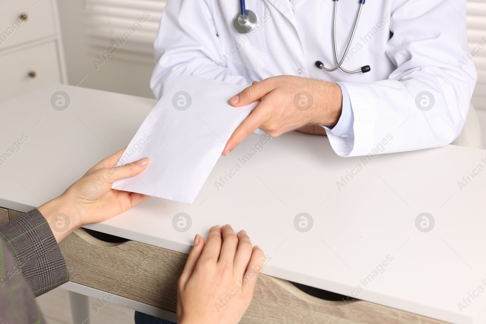 Photo of Corruption concept. Woman giving envelope with money to doctor at white table, closeup