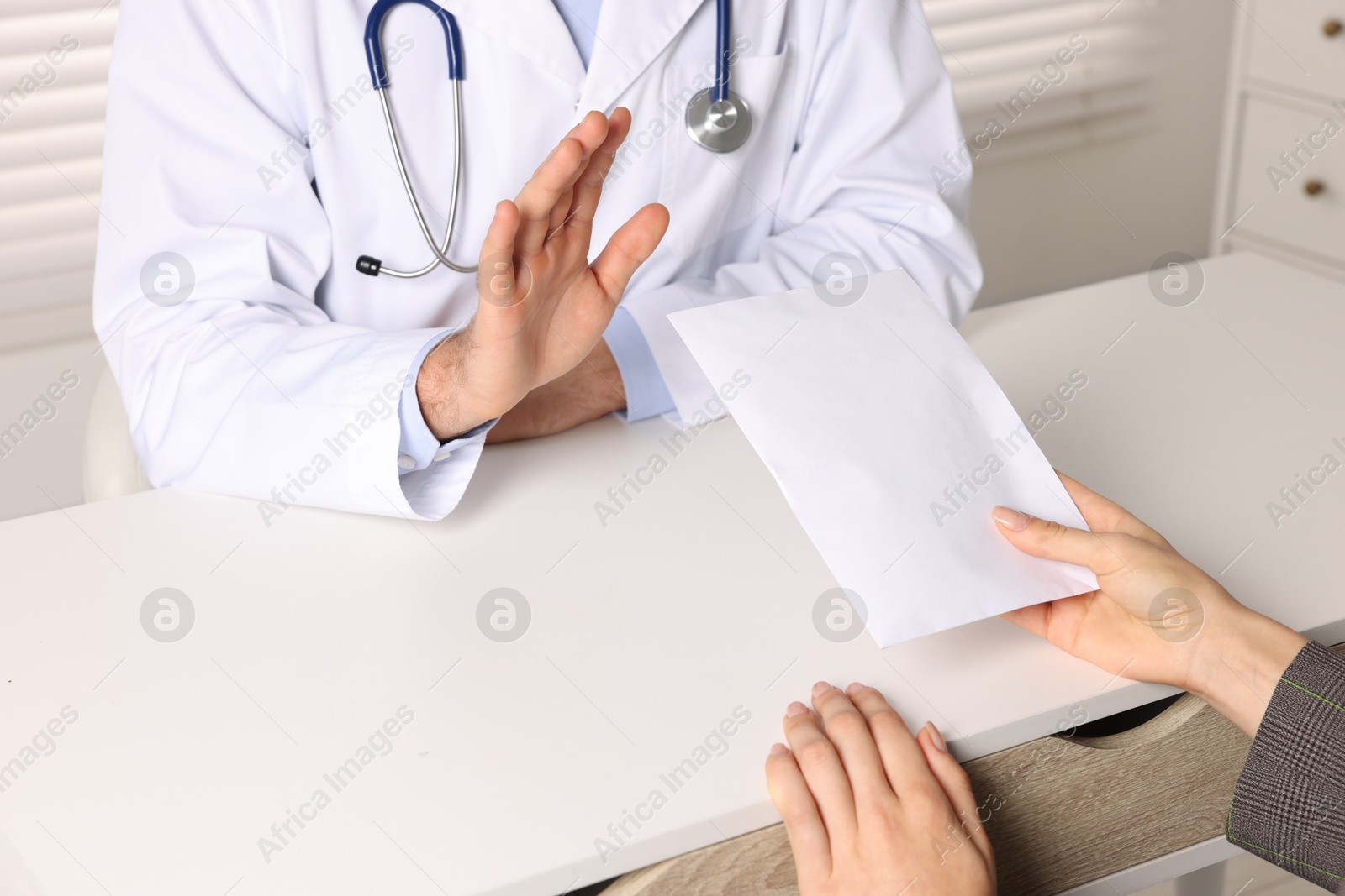 Photo of Corruption concept. Woman giving envelope with money to doctor at white table, closeup