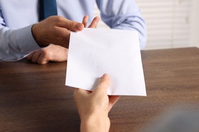 Photo of Corruption concept. Woman giving envelope with money to man at wooden table, closeup