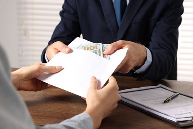 Photo of Corruption concept. Woman giving envelope with money to man at wooden table, closeup