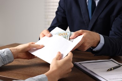 Photo of Corruption concept. Woman giving envelope with money to man at wooden table, closeup