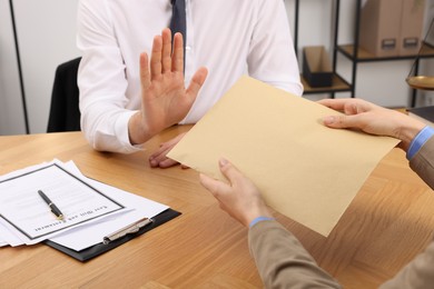 Photo of Corruption concept. Woman giving envelope with money to man at wooden table, closeup