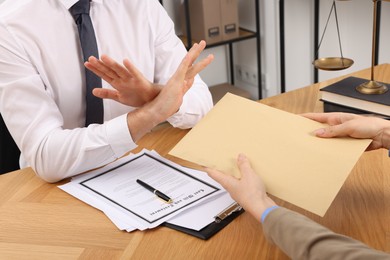 Photo of Corruption concept. Woman giving envelope with money to man at wooden table, closeup