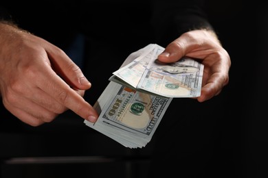 Photo of Corruption concept. Man holding dollar banknotes on black background, closeup