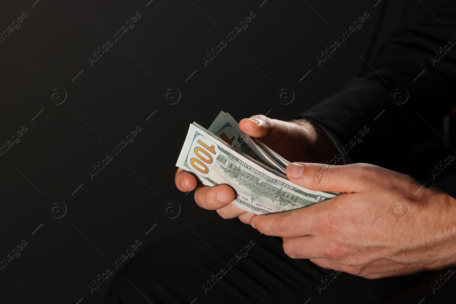 Photo of Corruption concept. Man holding dollar banknotes on black background, closeup