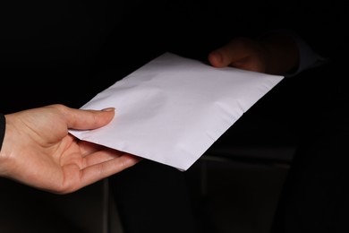 Photo of Corruption concept. Woman giving envelope with money to man on black background, closeup