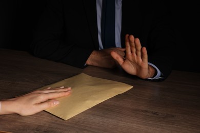 Photo of Corruption concept. Woman giving envelope with money to man at wooden table, closeup