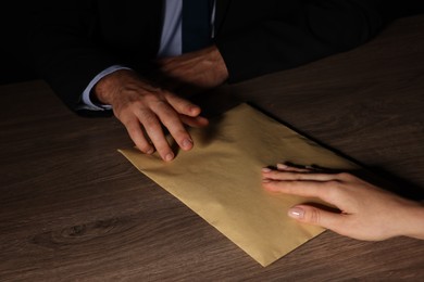 Photo of Corruption concept. Woman giving envelope with money to man at wooden table, closeup