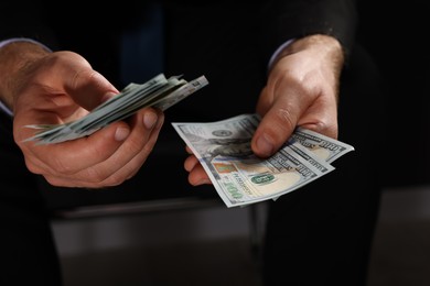 Photo of Corruption concept. Man holding dollar banknotes on black background, closeup