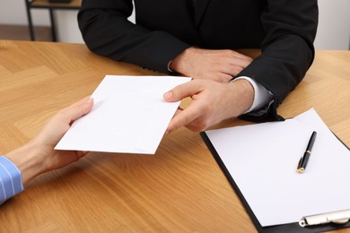 Photo of Corruption concept. Woman giving envelope with money to man at wooden table, closeup