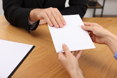 Photo of Corruption concept. Woman giving envelope with money to man at wooden table, closeup