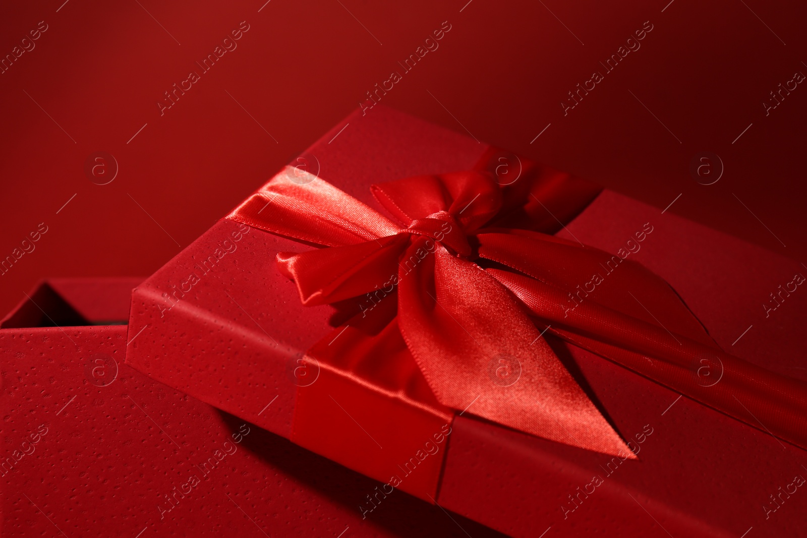 Photo of Red gift box on dark red background, closeup