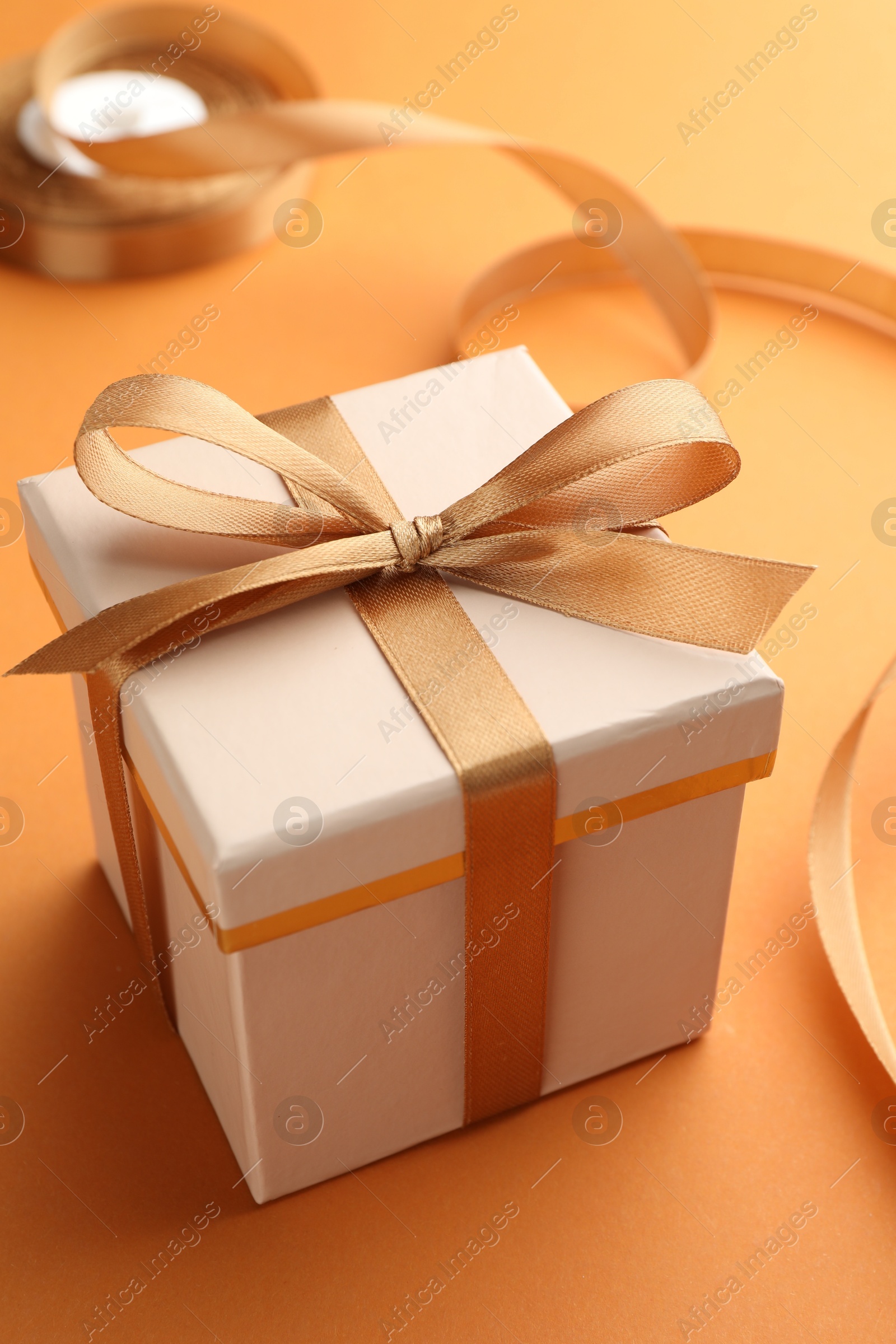 Photo of Beautiful gift box with golden bow on orange background, closeup