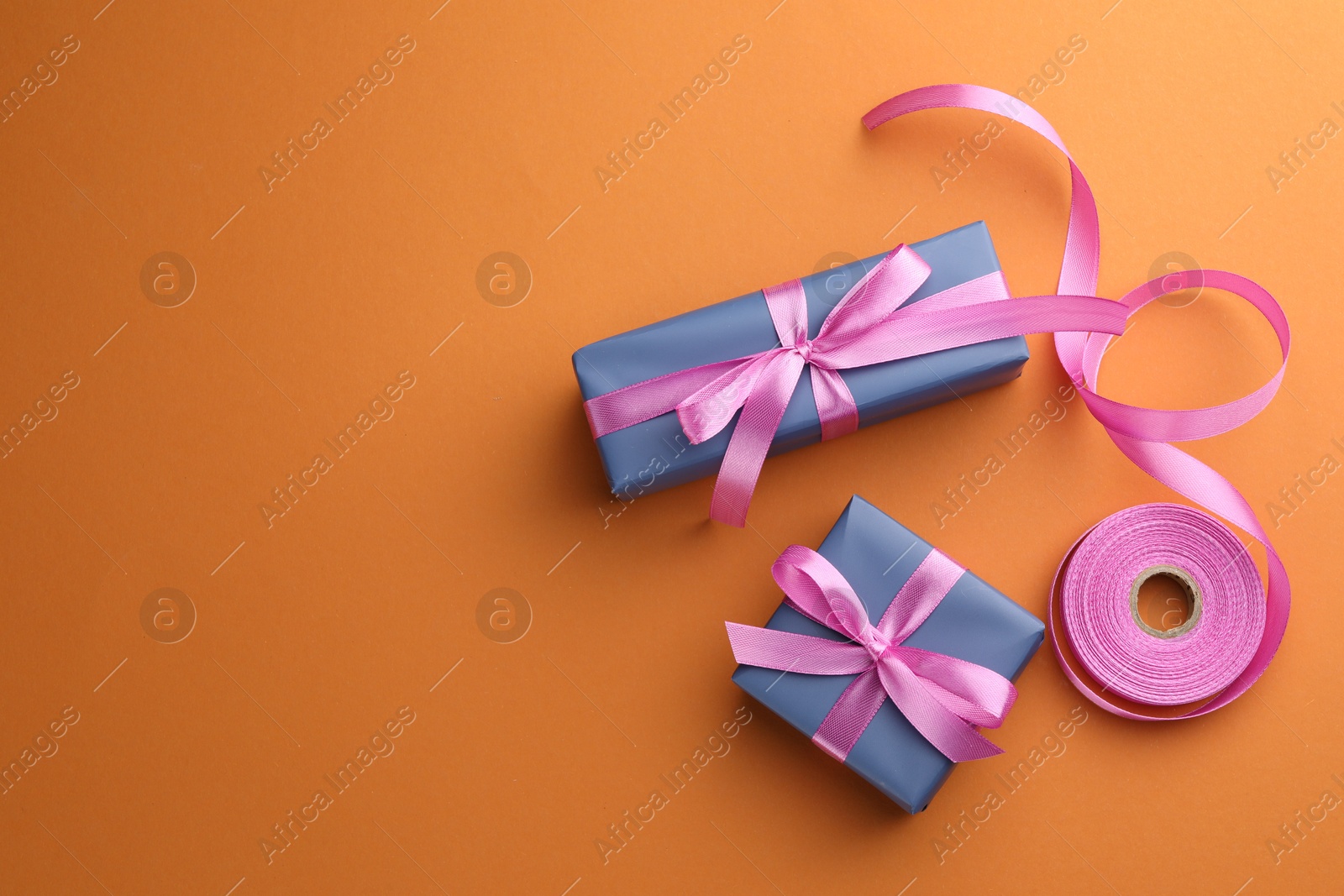 Photo of Beautiful gift boxes with pink bows on orange background, top view. Space for text