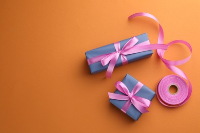 Beautiful gift boxes with pink bows on orange background, top view. Space for text