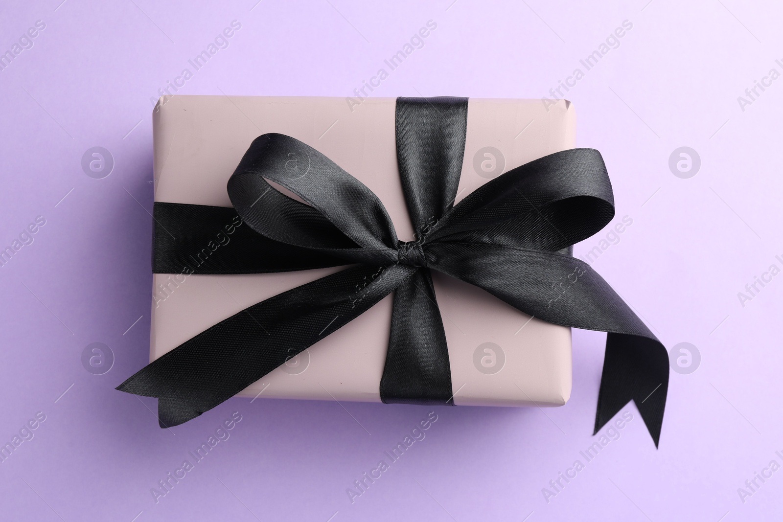 Photo of Beautiful gift box with black bow on violet background, top view