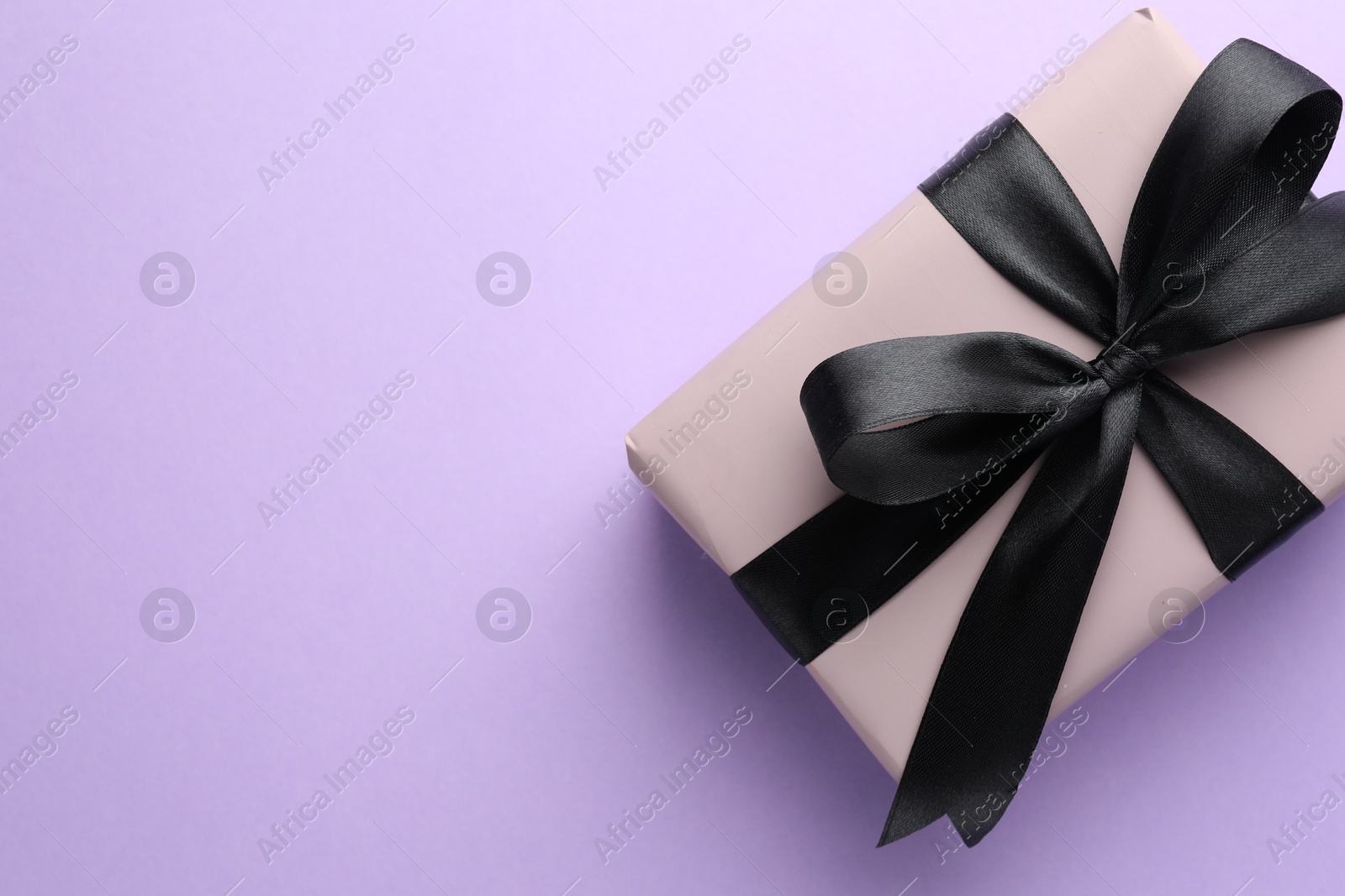 Photo of Beautiful gift box with black bow on violet background, top view. Space for text