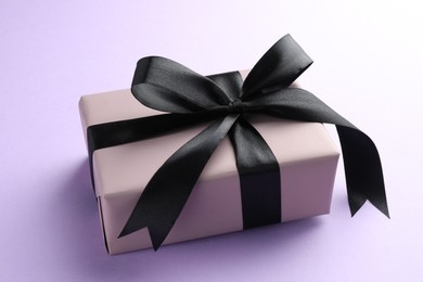 Beautiful gift box with black bow on violet background