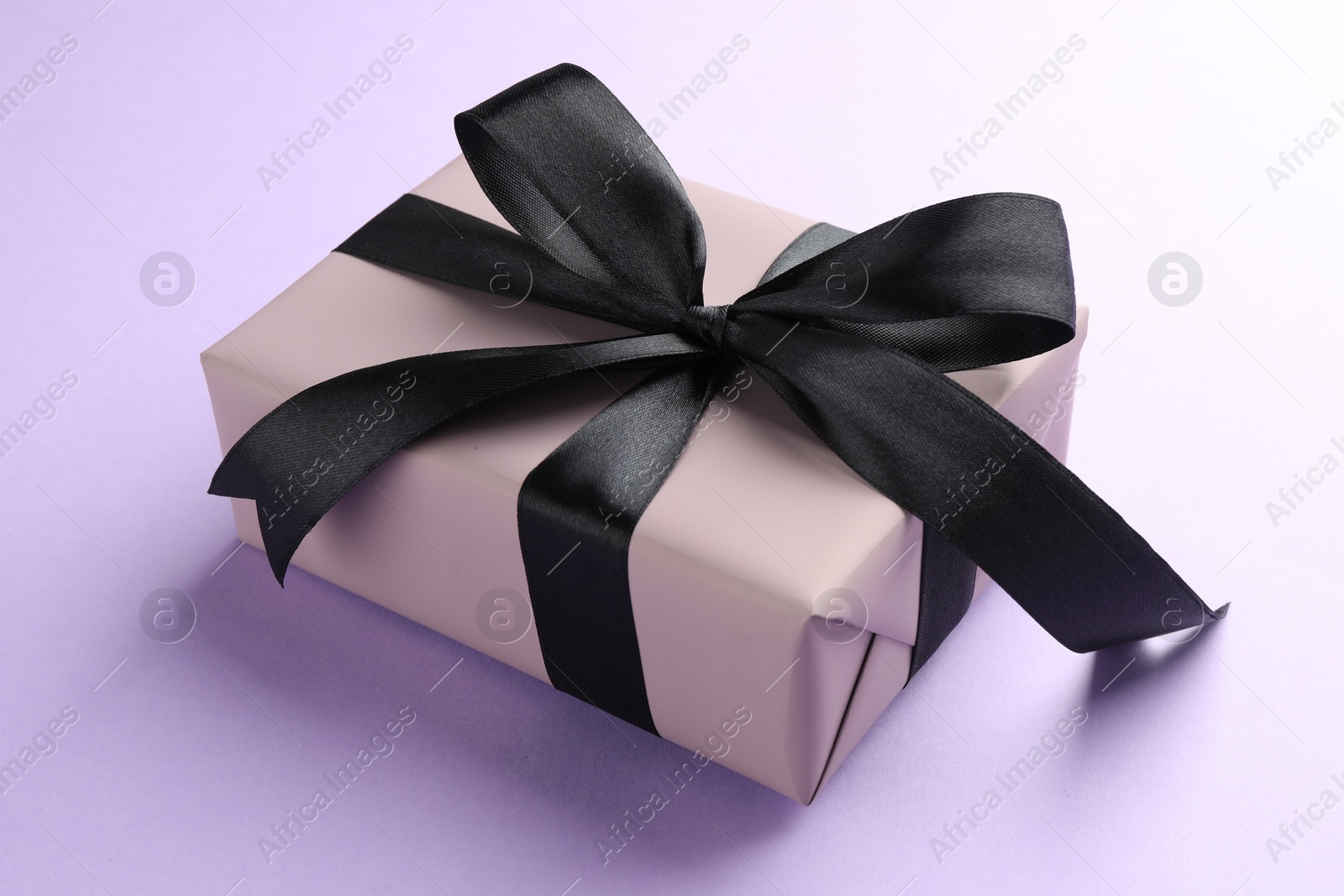 Photo of Beautiful gift box with black bow on violet background, closeup