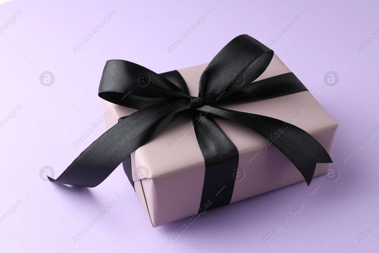 Photo of Beautiful gift box with black bow on violet background, closeup