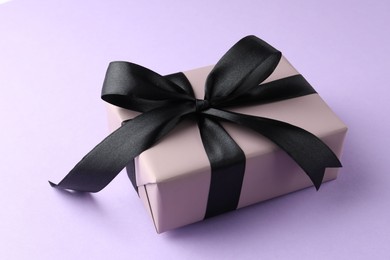 Beautiful gift box with black bow on violet background, closeup