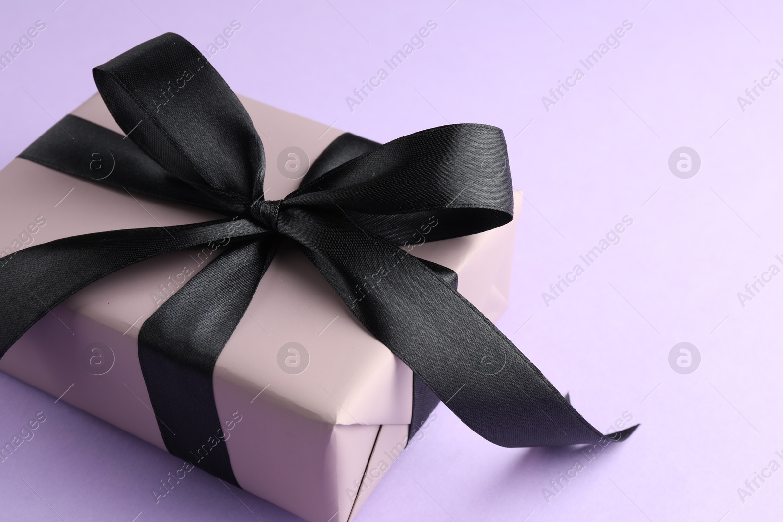 Photo of Beautiful gift box with black bow on violet background, closeup