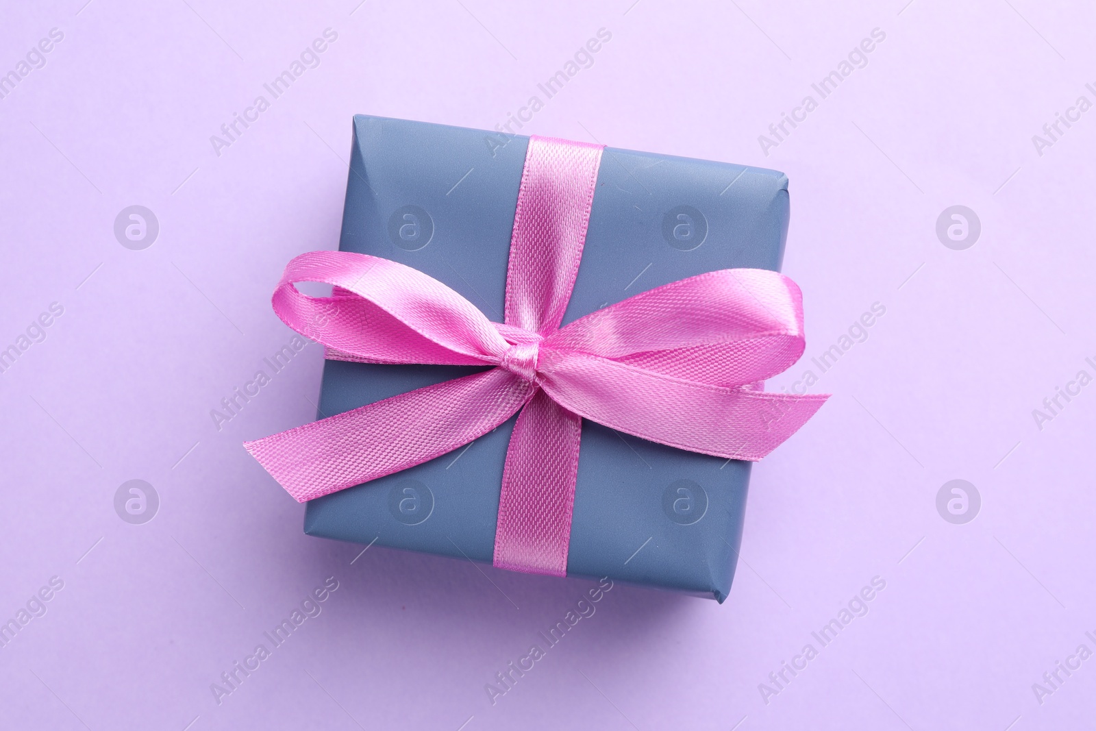 Photo of Beautiful gift box with pink bow on violet background, top view