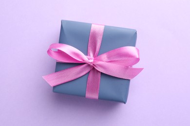 Beautiful gift box with pink bow on violet background, top view