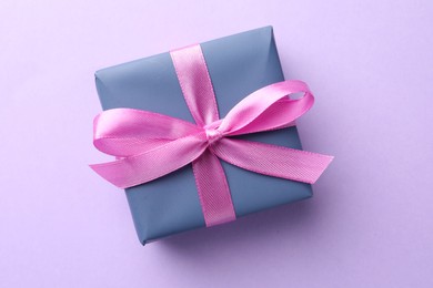 Photo of Beautiful gift box with pink bow on violet background, top view