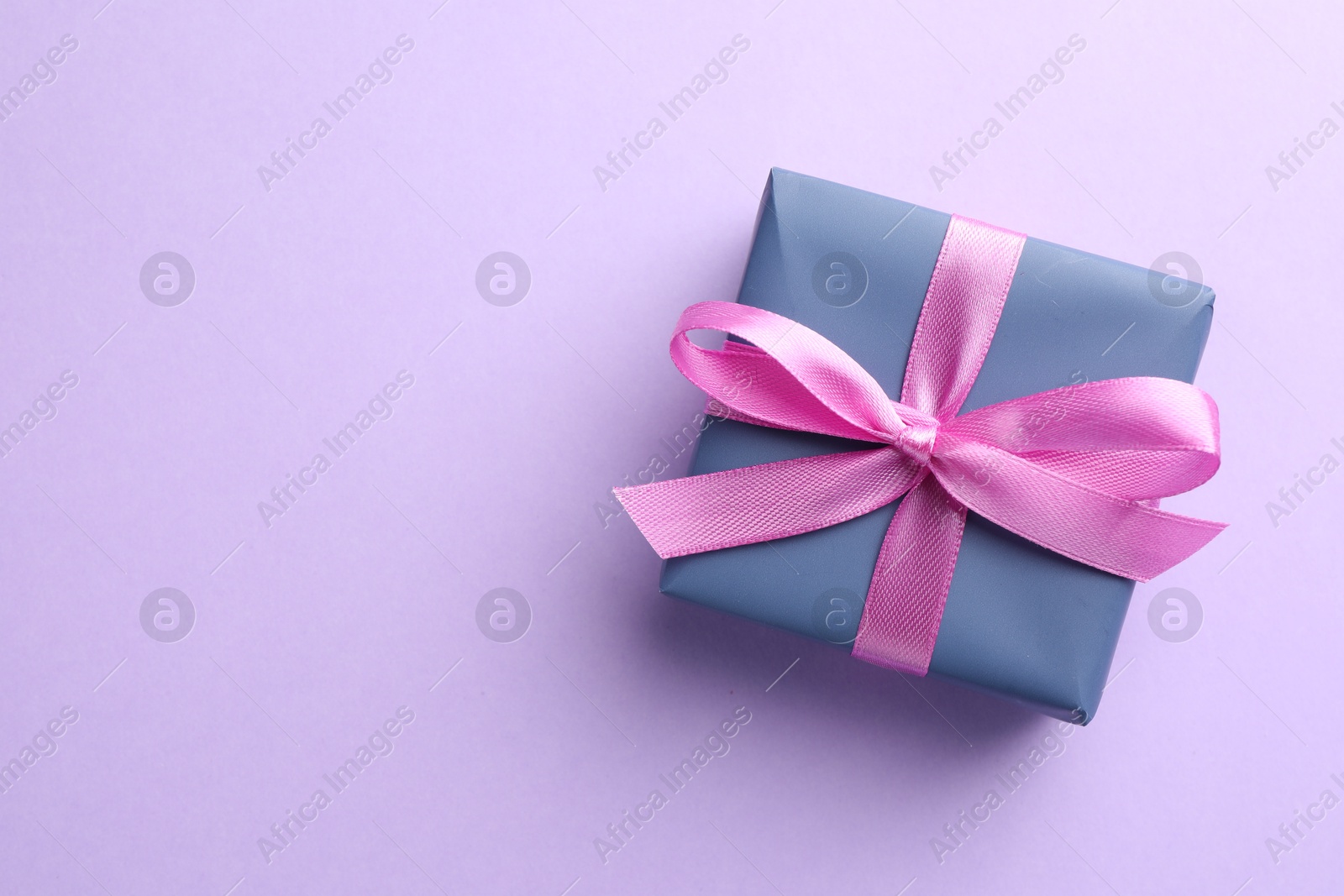 Photo of Beautiful gift box with pink bow on violet background, top view. Space for text