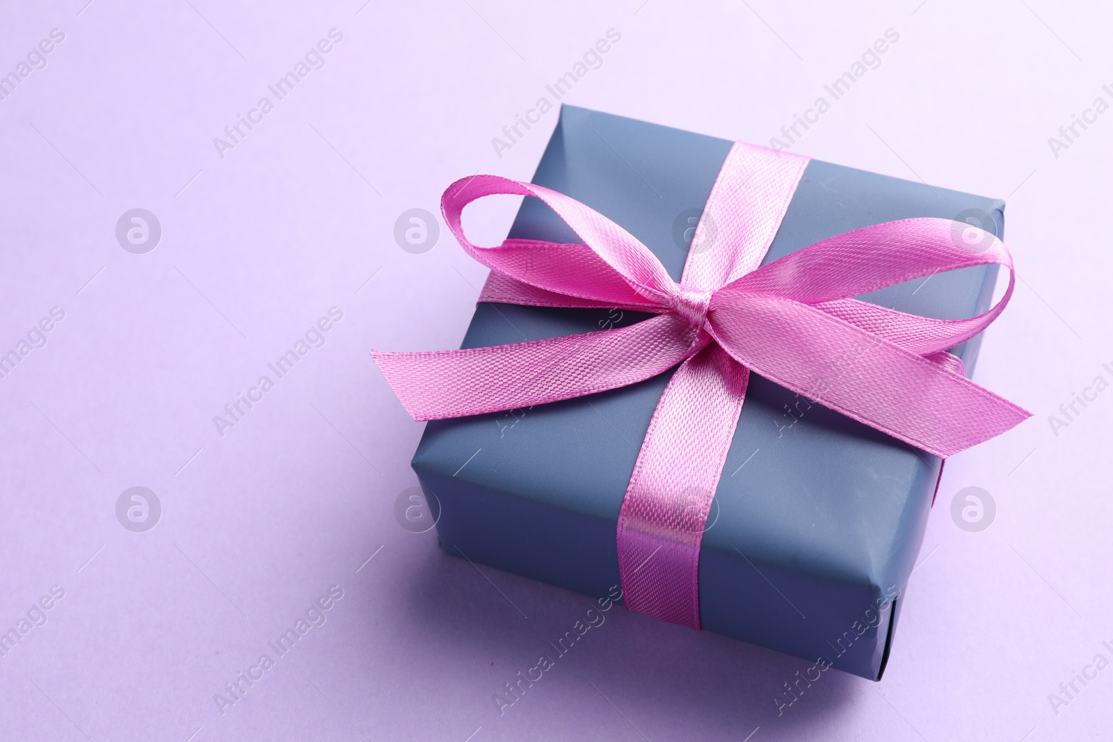 Photo of Beautiful gift box with pink bow on violet background, closeup. Space for text