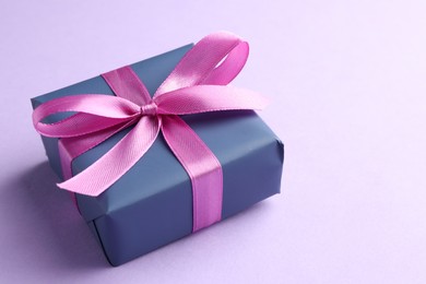 Beautiful gift box with pink bow on violet background, closeup. Space for text