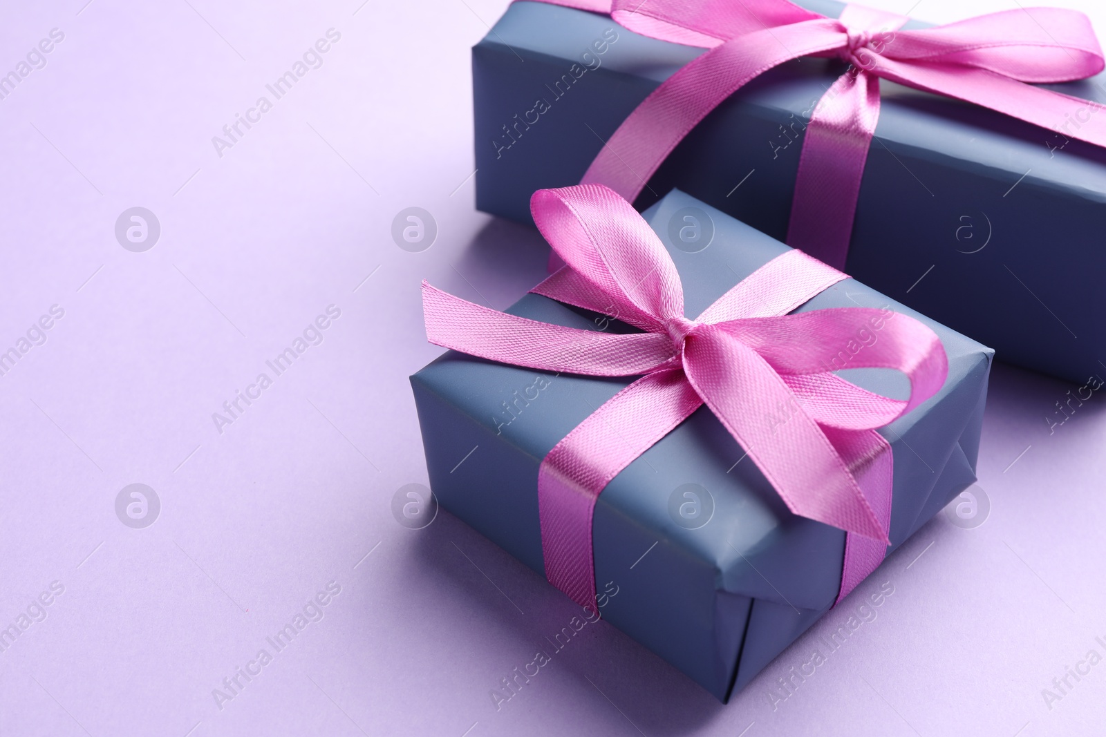 Photo of Beautiful gift boxes with pink bows on violet background, space for text