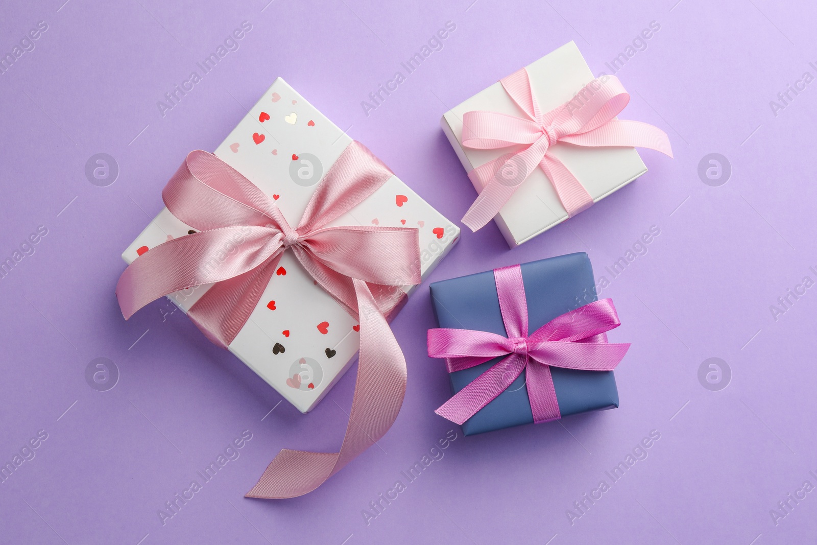 Photo of Beautiful gift boxes with pink bows on violet background, flat lay