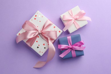 Photo of Beautiful gift boxes with pink bows on violet background, flat lay