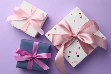 Beautiful gift boxes with pink bows on violet background, flat lay