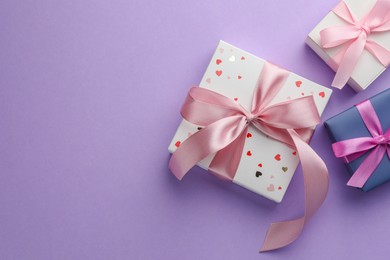 Beautiful gift boxes with pink bows on violet background, flat lay. Space for text