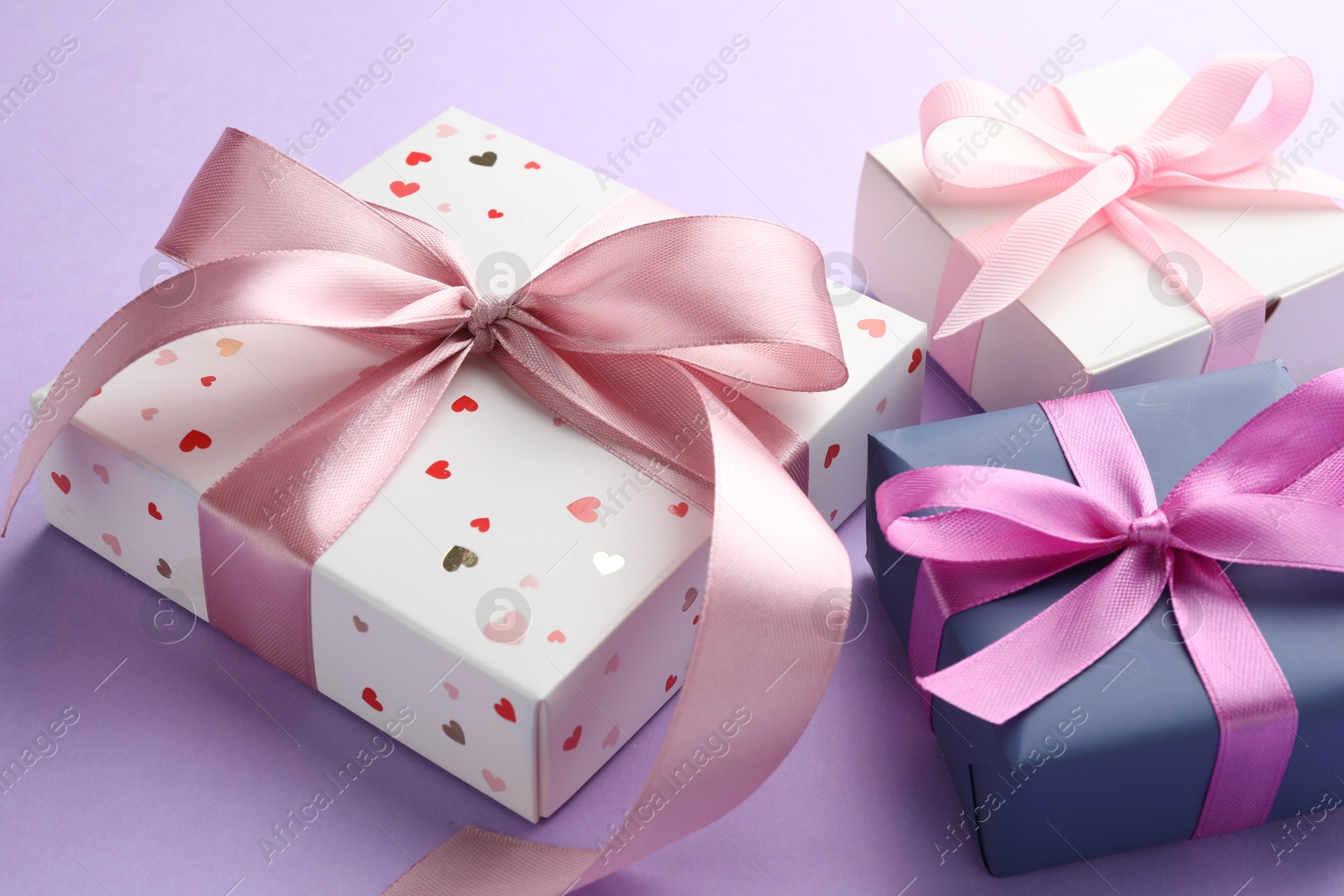 Photo of Beautiful gift boxes with pink bows on violet background, closeup