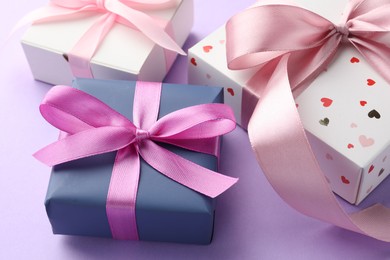 Photo of Beautiful gift boxes with pink bows on violet background, closeup