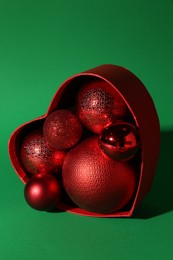 Photo of Red heart shaped box with Christmas balls on green background