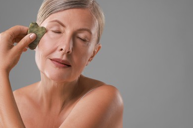 Beautiful woman doing facial massage with gua sha tool on grey background. Space for text